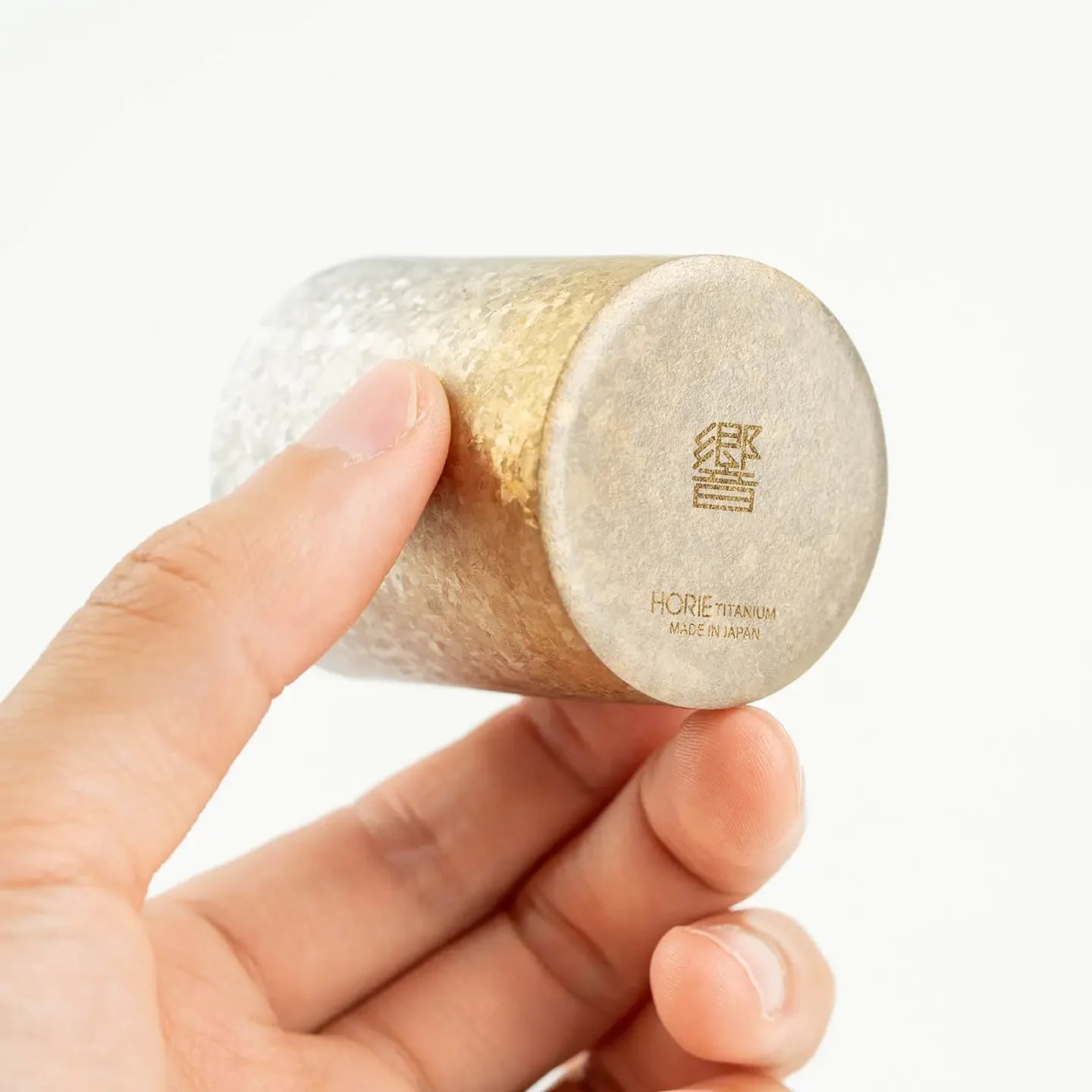 A hand holding the base of the HORIE Titanium Sake Cup to show the bottom craftsmanship.