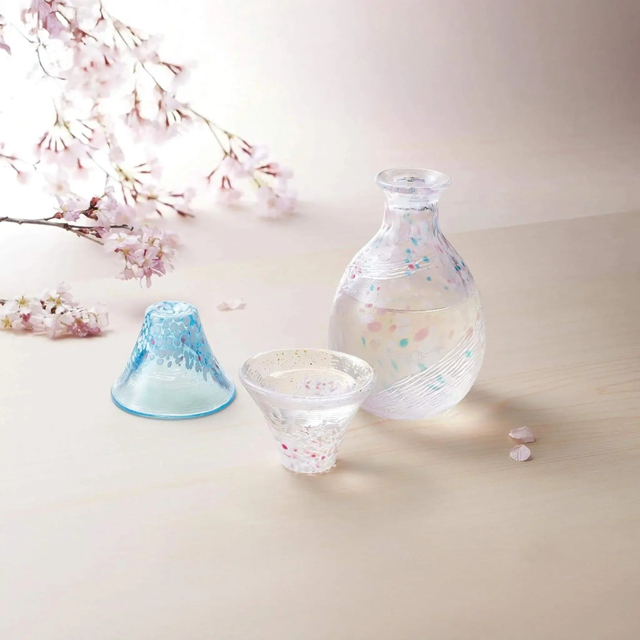 Japanese sake set with cherry blossom and Mount Fuji design, handmade glass cups and bottle displayed in spring sakura scene.