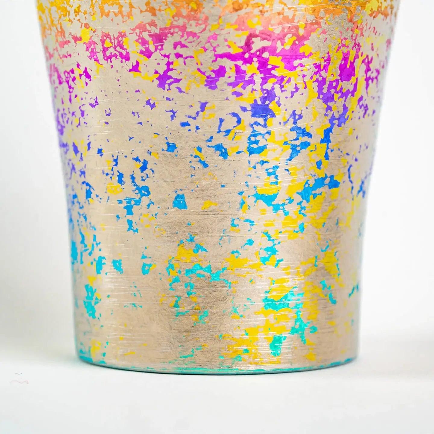 Close-up detail of the titanium tumbler's surface with vibrant, multicolored (yellow, purple, blue, cyan) rainbow splatter finish.